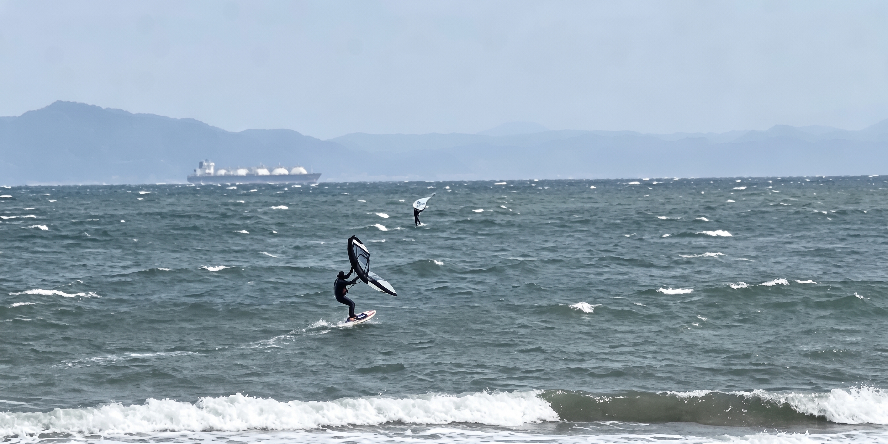 葉山の沖でウイングフォイルを楽しむ人たちと、沖を行くタンカー